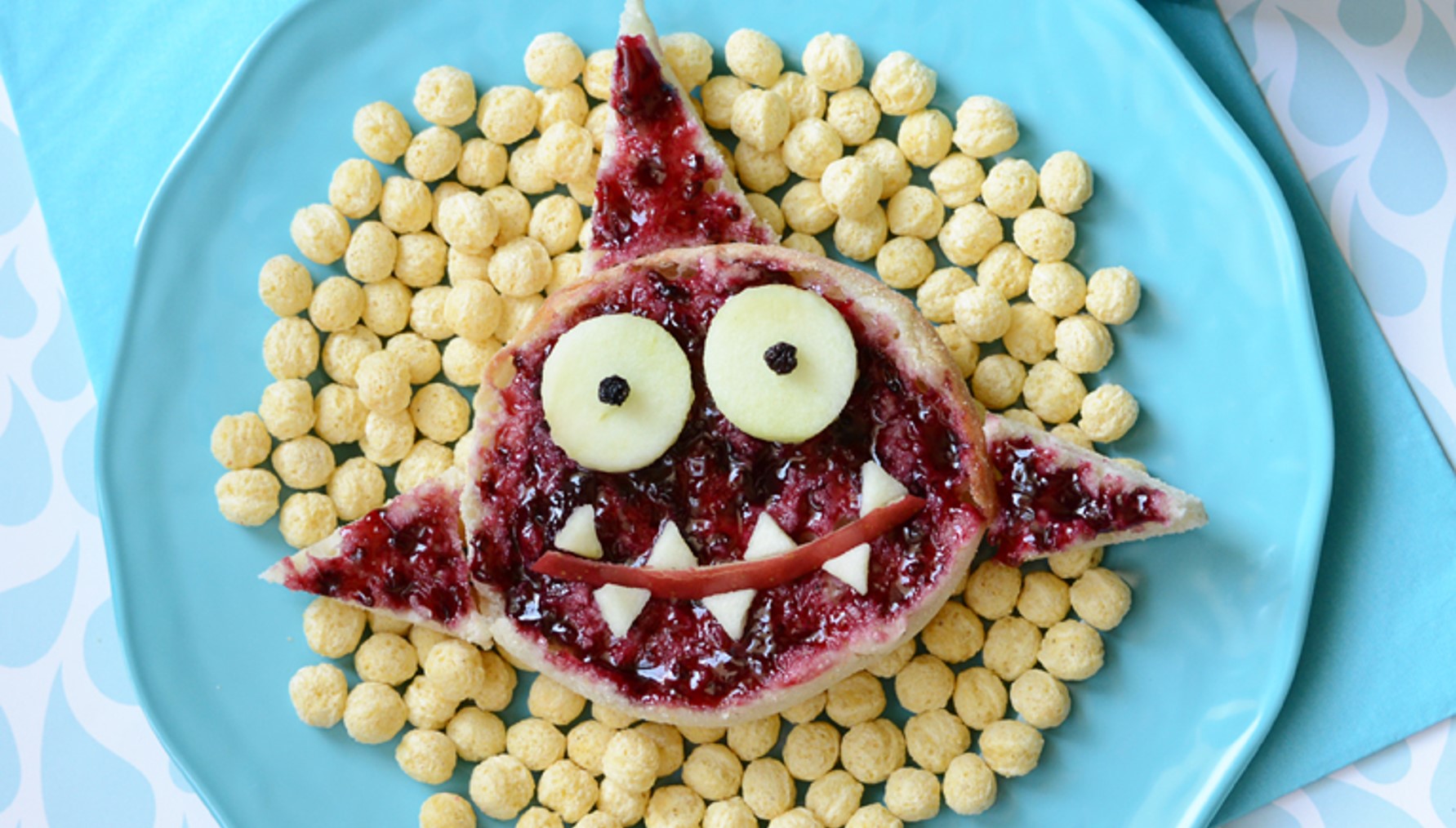 Kix cereal pieces on a blue plate with a jelly toast shaped like a friendly shark on top of them