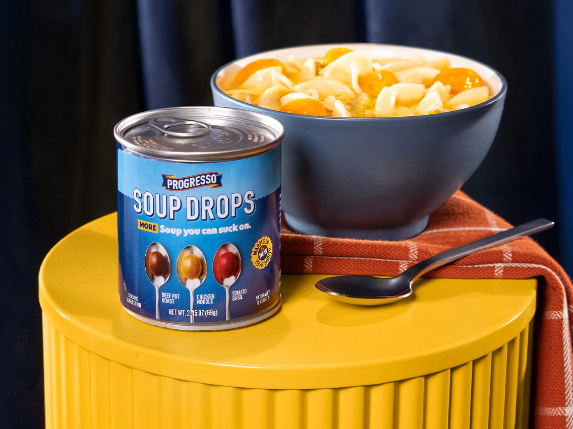 Progresso Soup Drops Variety Pack in front of spoon and a bowl of Progresso Chicken Noodle Soup​, all atop a yellow table.​